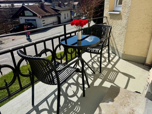 Kleine Terrasse mit runden Tisch, zwei Stühlen und einer Vase mit roten Blumen.