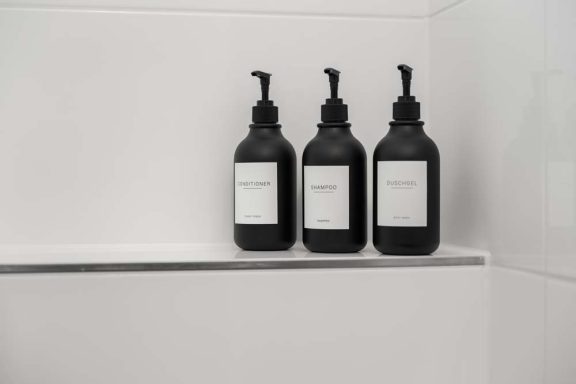 Drei schwarze Flaschen mit weißen Etiketten auf einem Regal in der Dusche.