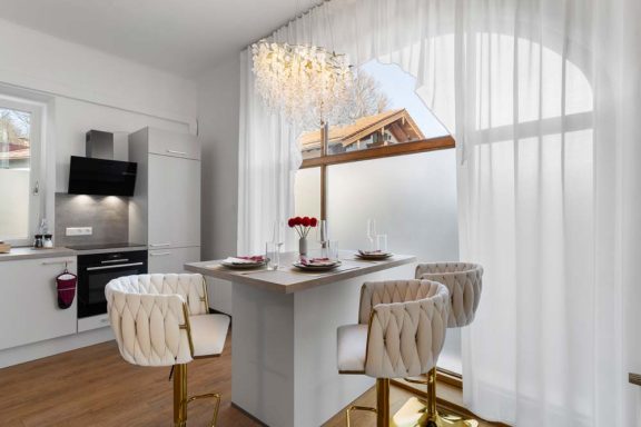 Helle Küche mit Esstisch und Stühlen, großen Fenstern und eleganter Beleuchtung.