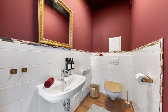 Kleines, elegantes Badezimmer mit Waschbecken, Toilette und rotem Wände.