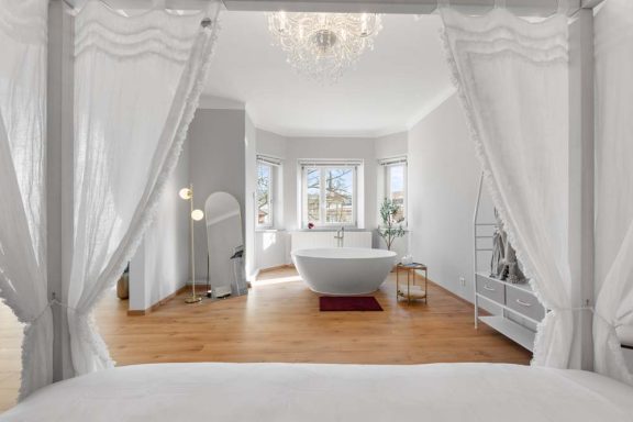 Helles, elegantes Schlafzimmer mit Badewanne und Fensterblick.
