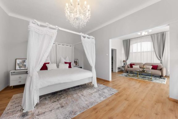 Helles Schlafzimmer mit einladendem Himmelbett und gemütlichem Wohnzimmer im Hintergrund.